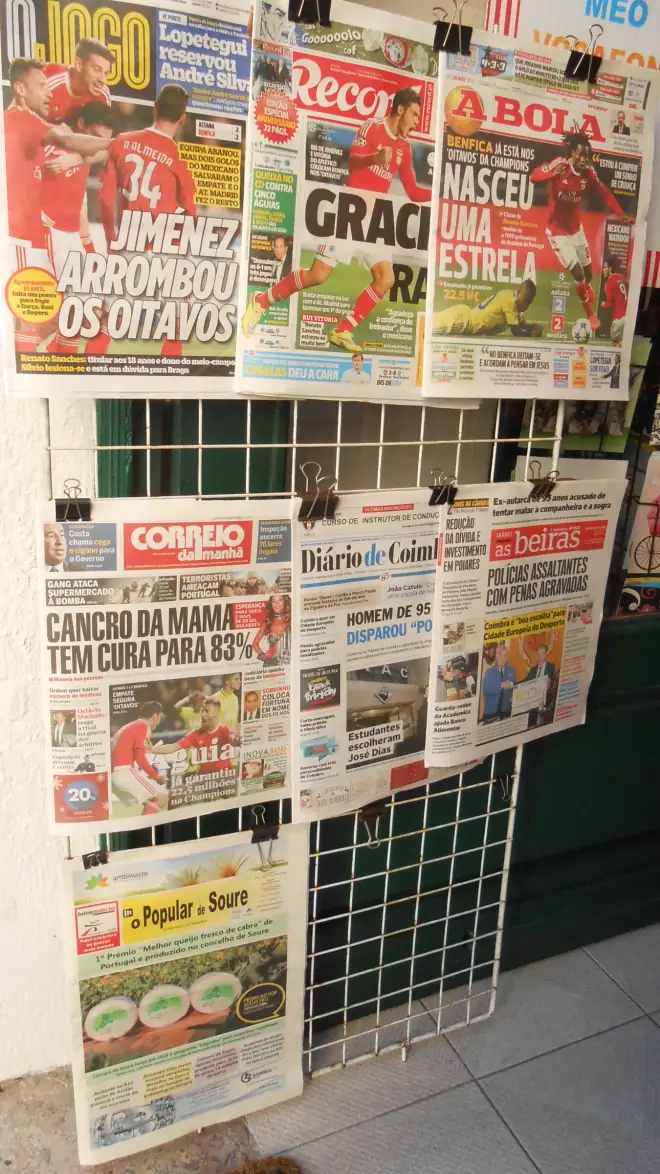 Expositor de rede numa papelaria com as capas de O Jogo, Record e A Bola na fila de cima e jornais generalistas e regionais por baixo